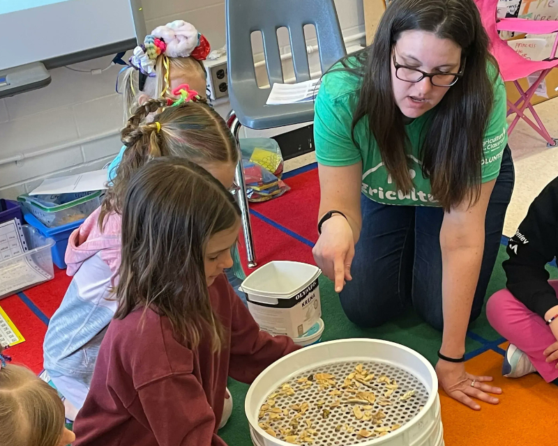 Woman volunteer pointing and showing students a seed bucket
